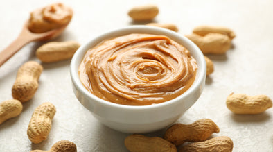 Peanut butter dogs can eat / Can dogs eat peanut butter? Image of peanut butter on a spoon and in a bowl surrounded by monkey nuts.