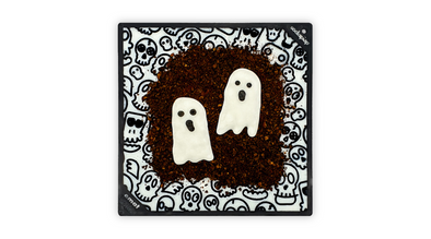 Black dog lick mat with a zombie and skull pattern filled with white milk kefir. Topped with liver cake crumb and two frozen yoghurt ghost dog halloween treats. 